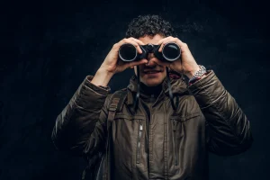Entrepreneur in Malaysia looking through binoculars while smiling with black background.
